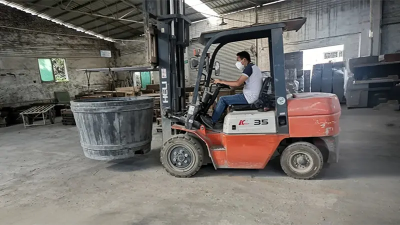 Heavy industrial forklift safely transporting a giant custom GRC municipal planter utilizing base-integrated channels.